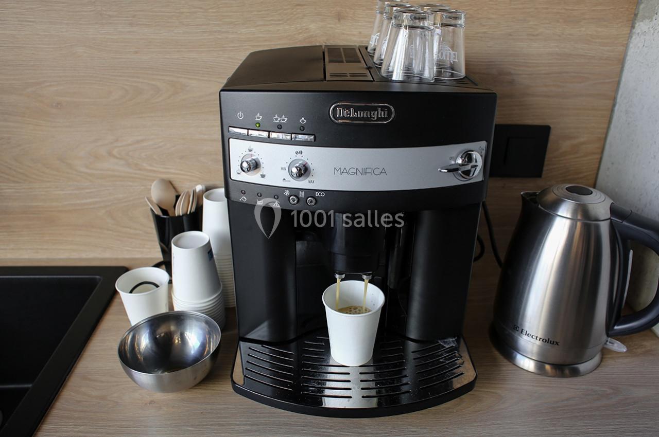 Machine à café automatique avec gobelet en cours de remplissage, posée sur un plan de travail avec accessoires à proximité.