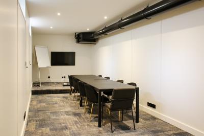 Salle de réunion moderne avec table noire, chaises, écran mural, tableau blanc et éclairage encastré.