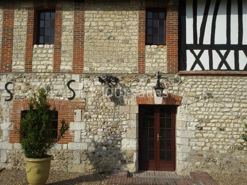 Façade en pierre et briques d'un bâtiment ancien avec une porte en bois, fenêtres à petits carreaux et un pot de plante.