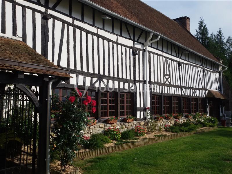 Maison à colombages avec façade blanche et poutres noires, entourée de fleurs et d'un jardin bien entretenu.