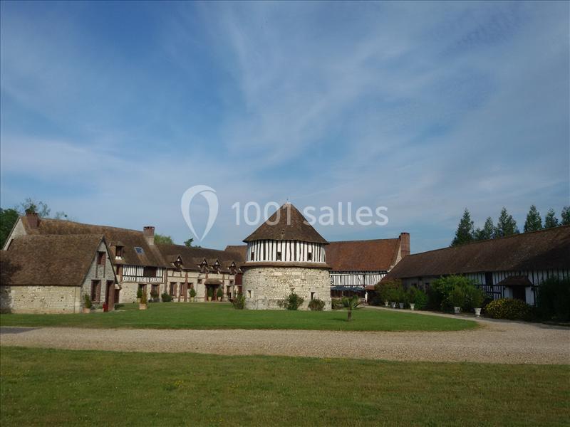 Bâtiments traditionnels à colombages entourant une cour avec pelouse, sous un ciel partiellement nuageux.