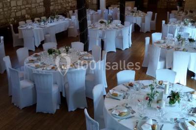 Salle de réception décorée avec des tables rondes dressées, des lanternes suspendues et un éclairage tamisé.
