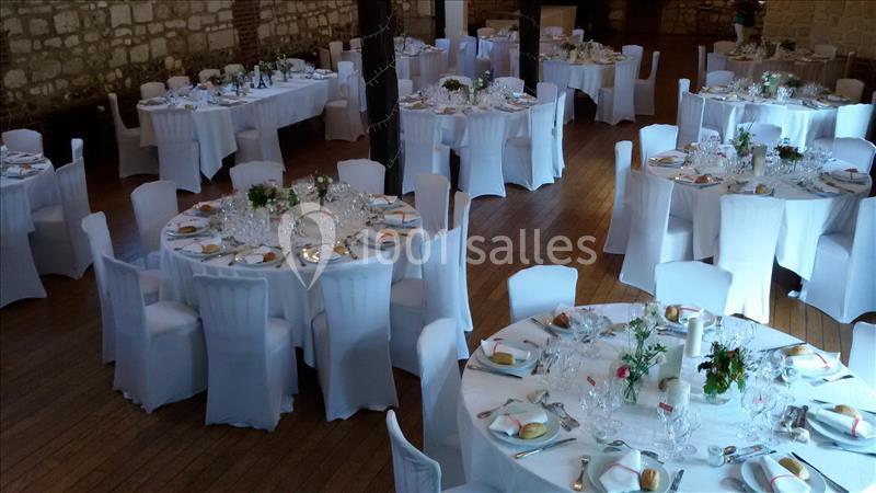 Salle de réception avec tables rondes dressées, nappes blanches, chaises assorties et décorations florales.