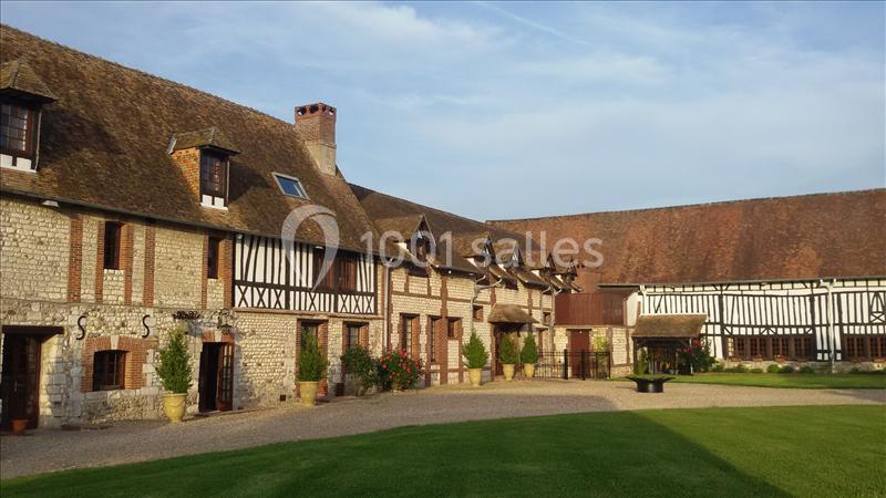 Bâtiment à colombages et en pierre avec cour pavée et pelouse, sous un ciel dégagé.