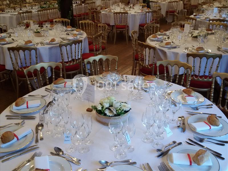 Salle de réception avec tables rondes dressées, nappes blanches, couverts élégants et centres de table fleuris.