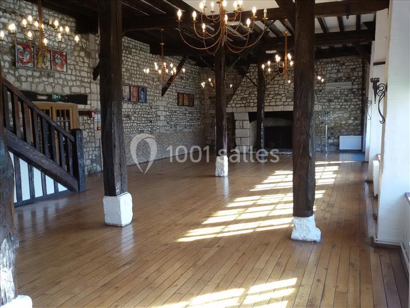 Salle spacieuse avec parquet en bois, poutres apparentes, murs en pierre et lustres suspendus.