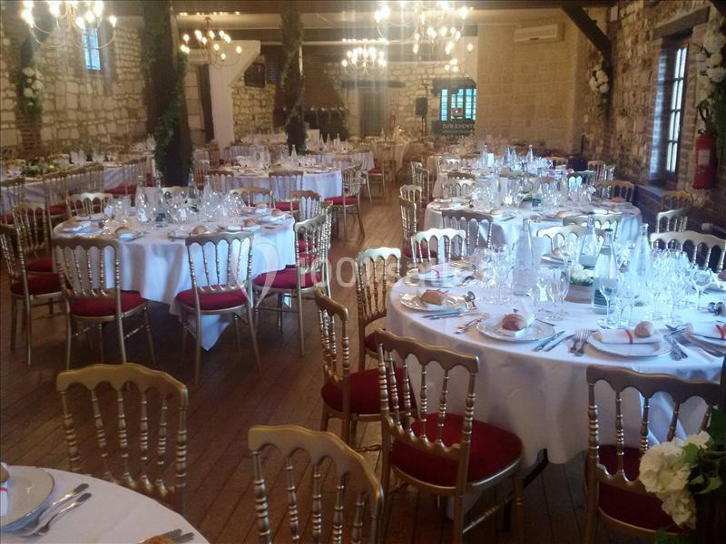 Salle de réception décorée avec des tables rondes dressées, chaises dorées et éclairage chaleureux.
