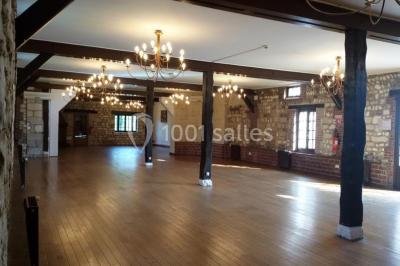Salle de réception décorée avec des tables rondes dressées, des lanternes suspendues et un éclairage tamisé.