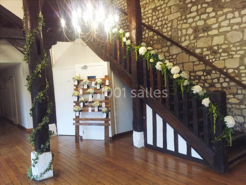 Escalier en bois décoré de guirlandes de fleurs blanches et feuillage, dans une pièce aux murs en pierre apparente.