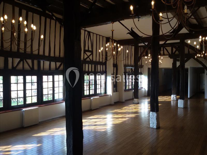 Salle lumineuse avec poutres apparentes, parquet en bois et grandes fenêtres laissant entrer la lumière naturelle.