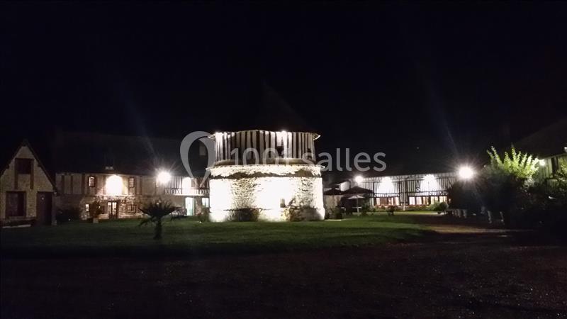 Bâtiments à colombages et tour centrale éclairés la nuit, entourés d'une pelouse et d'une cour.