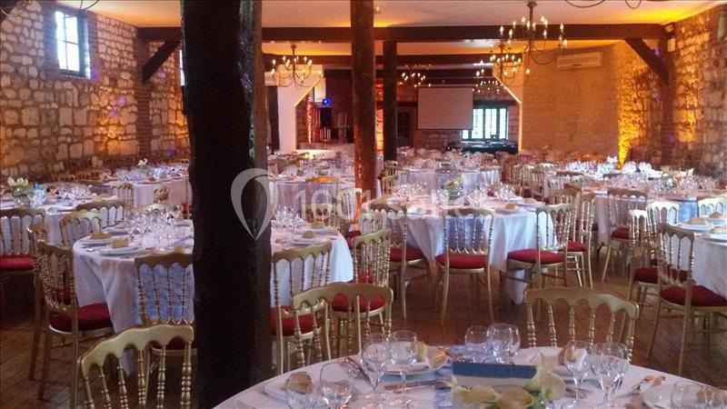 Salle de réception en pierre avec tables rondes dressées, chaises dorées et éclairage chaleureux.