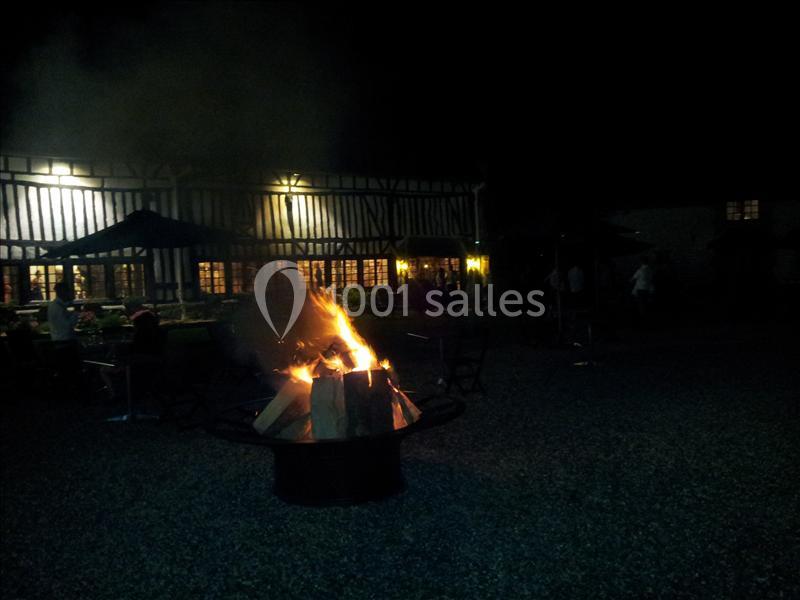 Un feu de camp allumé dans une cour sombre devant un bâtiment à colombages éclairé.