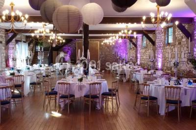 Salle de réception décorée avec des tables rondes dressées, des lanternes suspendues et un éclairage tamisé.