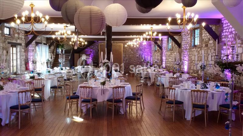 Salle de réception décorée avec des tables rondes dressées, des lanternes suspendues et un éclairage tamisé.