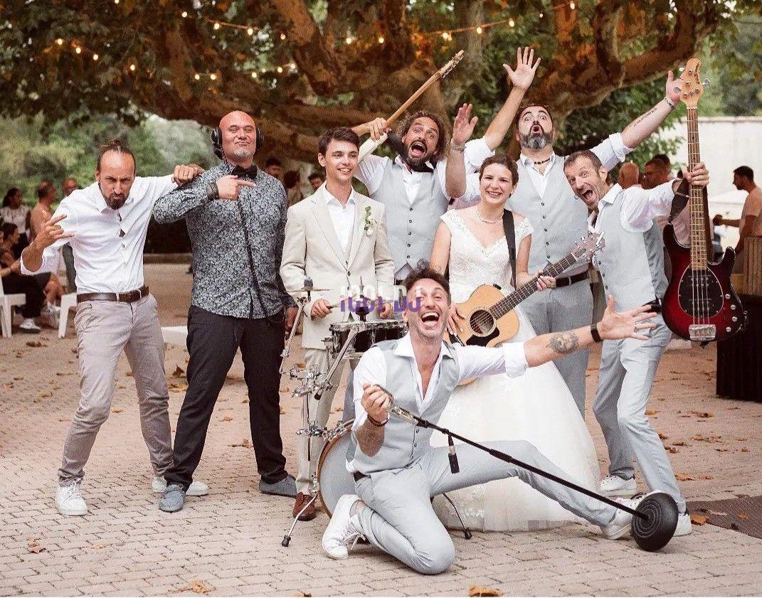 Un groupe de musiciens et une mariée posent joyeusement avec des instruments sous un grand arbre décoré de lumières.