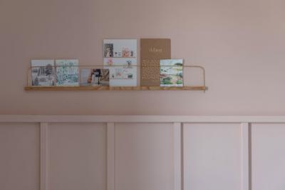 Chambre moderne avec lit double, mur rose, bureau en bois clair, chaise noire et éclairage mural.