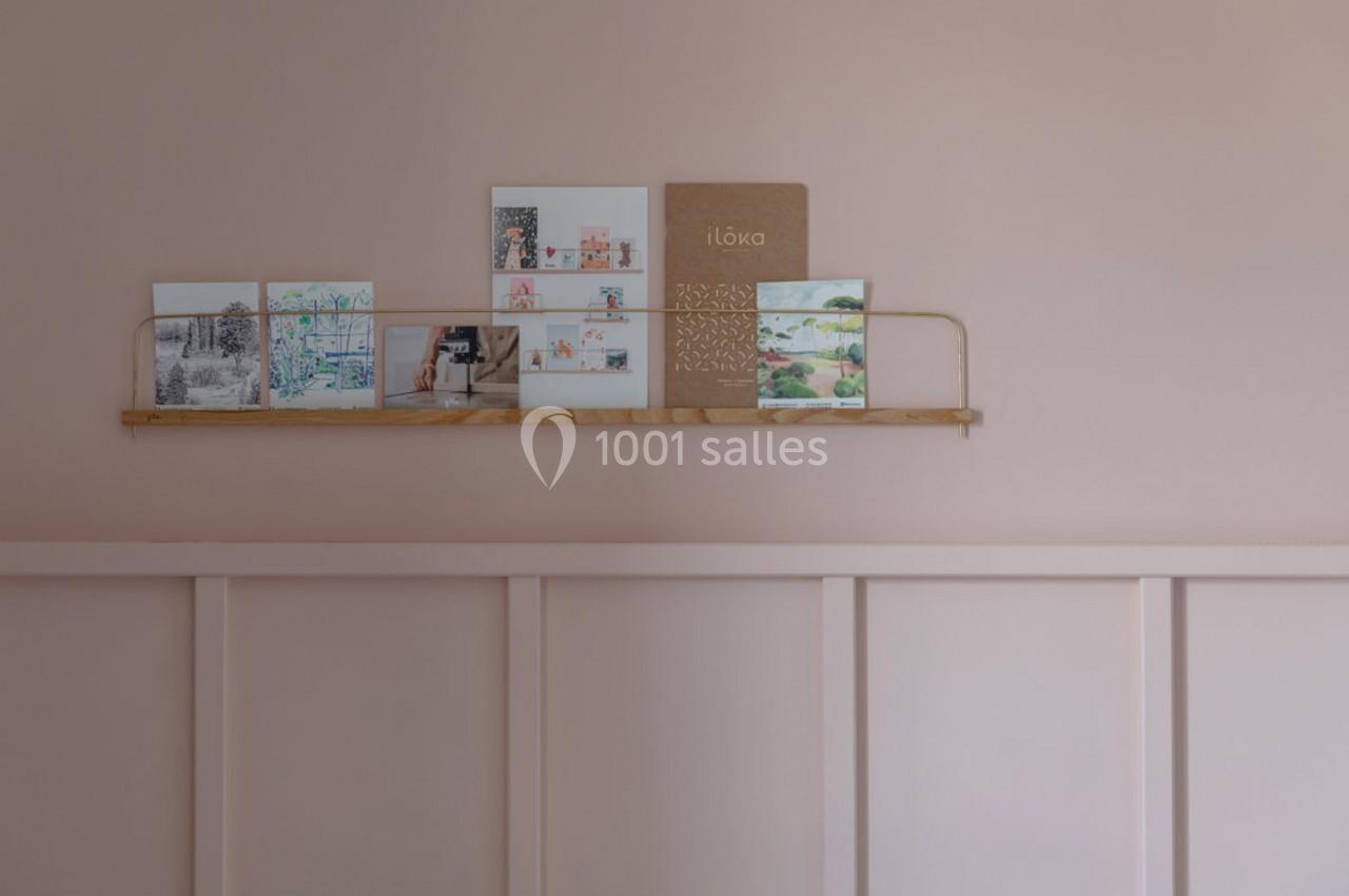 Étagère murale en bois clair avec des cartes illustrées et un carnet beige, sur un mur rose pastel.