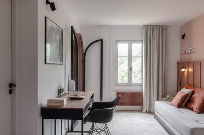 Chambre moderne avec lit double, mur rose, bureau en bois clair, chaise noire et éclairage mural.