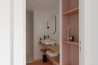 Chambre moderne avec lit double, mur rose, bureau en bois clair, chaise noire et éclairage mural.