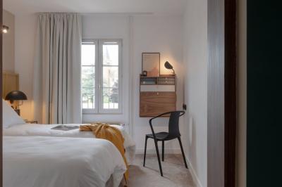 Chambre moderne avec lit double, mur rose, bureau en bois clair, chaise noire et éclairage mural.