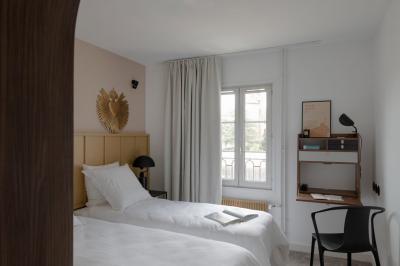 Chambre moderne avec lit double, mur rose, bureau en bois clair, chaise noire et éclairage mural.