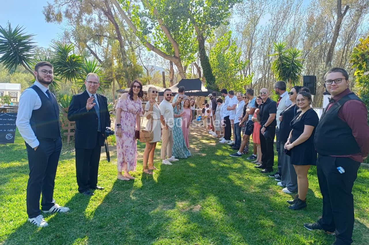 Groupe de personnes alignées en extérieur, sur une pelouse, entourées d'arbres et de végétation.