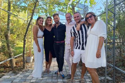 Une femme lit un discours devant un couple assis sous une arche décorée, lors d'une cérémonie en extérieur.