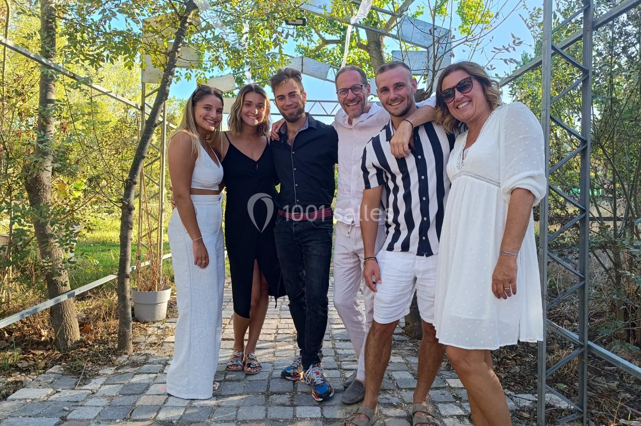 Un groupe de six personnes souriantes posant ensemble en extérieur, entouré de végétation et de structures métalliques.