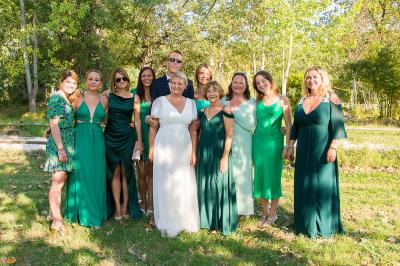 Une femme lit un discours devant un couple assis sous une arche décorée, lors d'une cérémonie en extérieur.