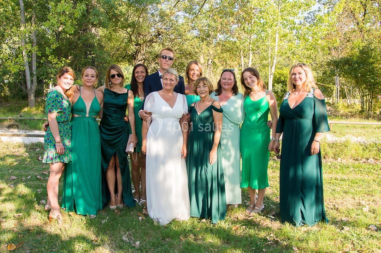 Un groupe de personnes posant en extérieur, certaines en robes vertes et une en robe blanche, dans un cadre arboré.