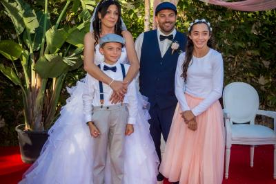 Une femme lit un discours devant un couple assis sous une arche décorée, lors d'une cérémonie en extérieur.