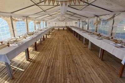 Une femme lit un discours devant un couple assis sous une arche décorée, lors d'une cérémonie en extérieur.