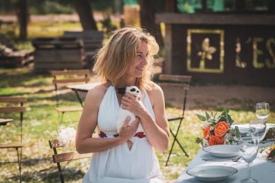 Une femme lit un discours devant un couple assis sous une arche décorée, lors d'une cérémonie en extérieur.