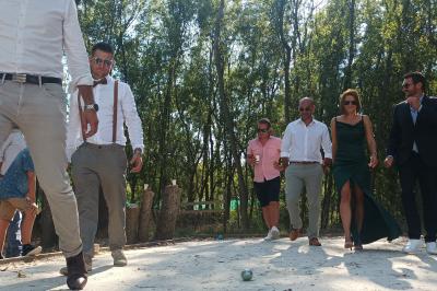 Une femme lit un discours devant un couple assis sous une arche décorée, lors d'une cérémonie en extérieur.