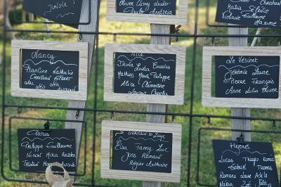 Une femme lit un discours devant un couple assis sous une arche décorée, lors d'une cérémonie en extérieur.