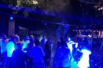 Une femme lit un discours devant un couple assis sous une arche décorée, lors d'une cérémonie en extérieur.