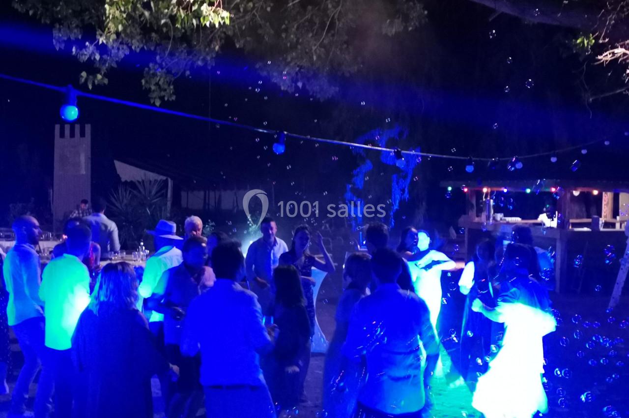 Des personnes dansent de nuit en extérieur sous des lumières bleues, entourées de bulles et d'une ambiance festive.