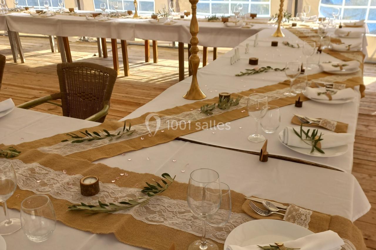 Tables décorées pour un événement avec nappes blanches, chemins de table en toile de jute, fleurs et vaisselle.