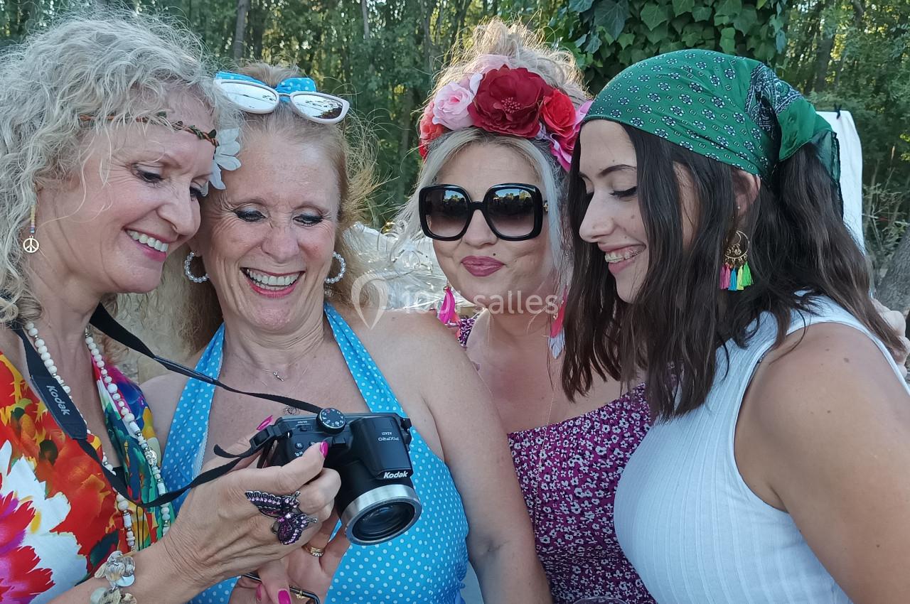 Quatre femmes souriantes regardent une photo sur un appareil photo dans un cadre extérieur boisé.