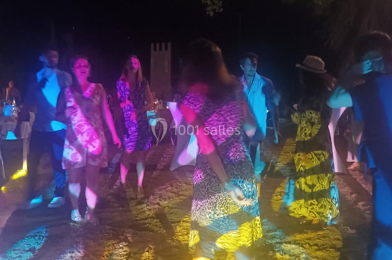 Des personnes dansent en groupe en extérieur, éclairées par des lumières colorées, dans une ambiance festive nocturne.