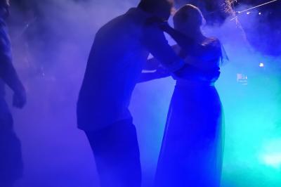 Une femme lit un discours devant un couple assis sous une arche décorée, lors d'une cérémonie en extérieur.