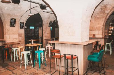 Salle voûtée en pierre avec des tables hautes, des tabourets colorés et un éclairage tamisé.