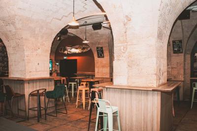 Salle voûtée en pierre avec des tables hautes, des tabourets colorés et un éclairage tamisé.