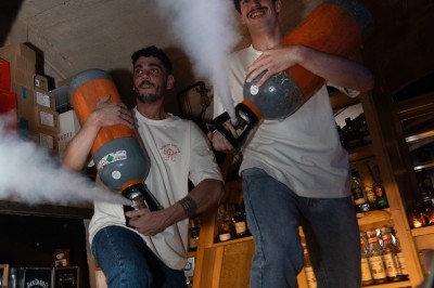 Deux hommes souriants sur un comptoir diffusent de la fumée avec des bonbonnes dans un bar.