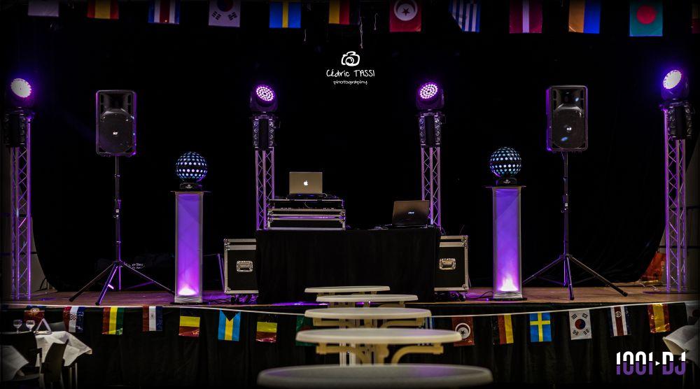 Configuration d'une scène avec des enceintes, des lumières colorées et une table de mixage, entourée de drapeaux…