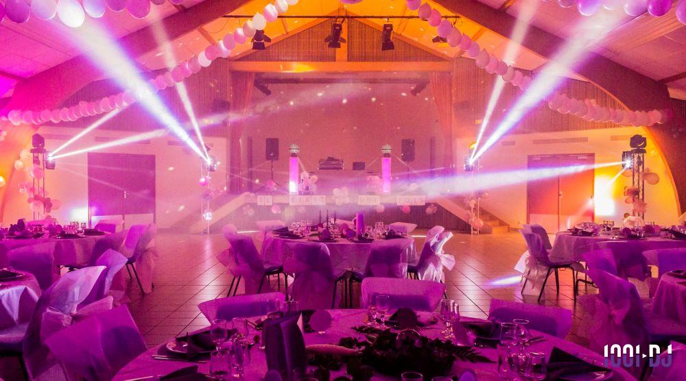 Salle de réception décorée avec des tables dressées et éclairages colorés, ambiance festive et lumineuse.