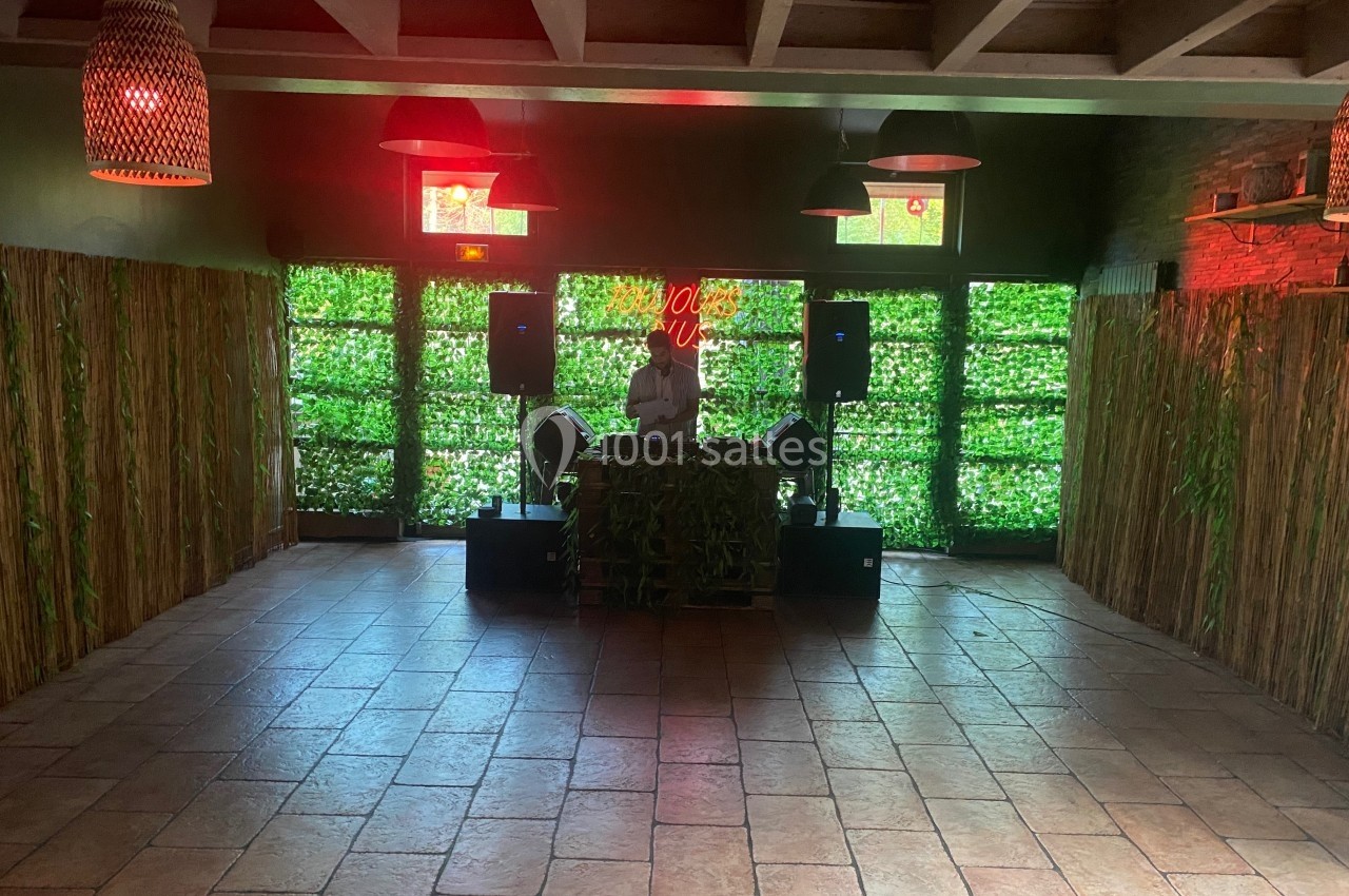 Un DJ joue de la musique dans une salle avec des murs végétalisés et un éclairage tamisé.