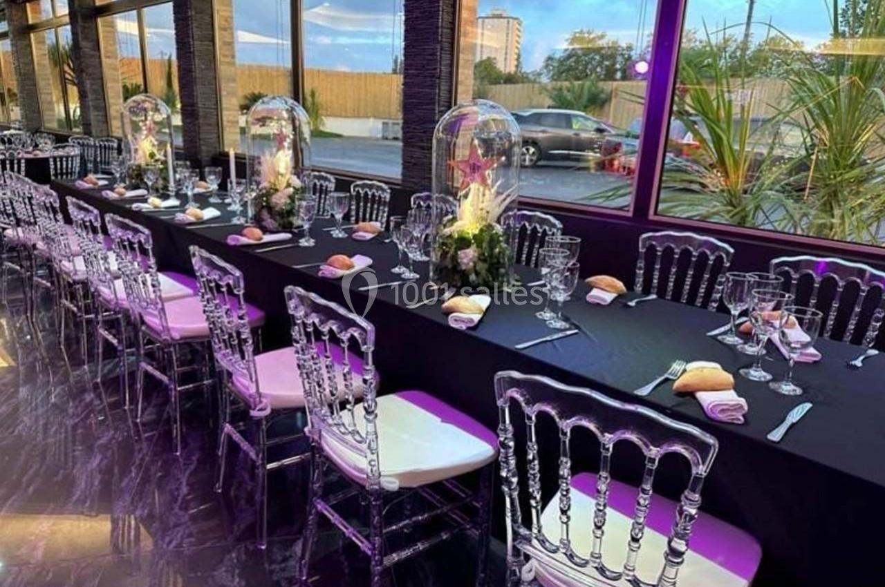 Salle de réception avec longues tables noires décorées de centres de table floraux et chaises transparentes.