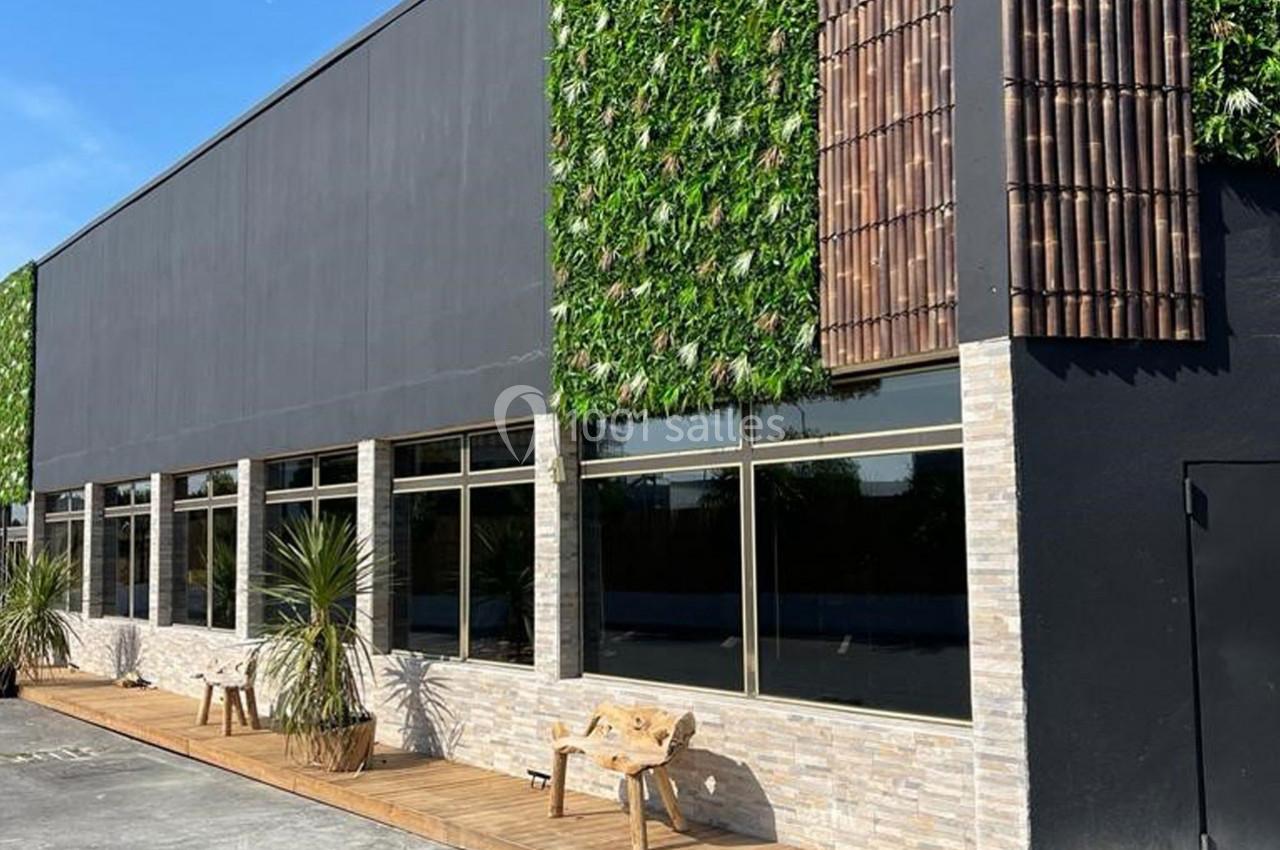 Façade moderne avec murs végétalisés, grandes fenêtres et bancs en bois sur une terrasse ensoleillée.